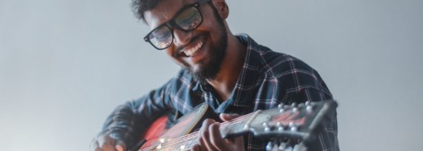 smiling man sitting while playing guitar